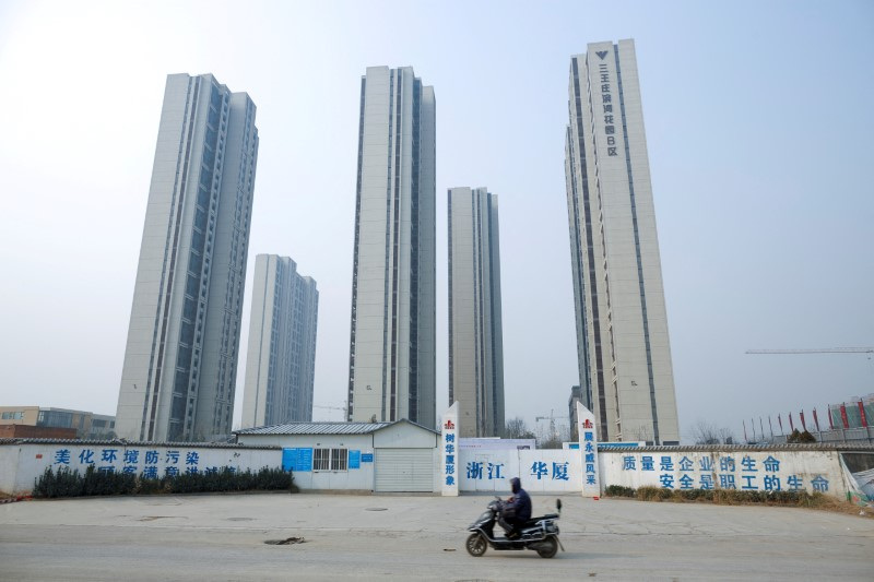 © Reuters. FILE PHOTO: A man rides a scooter past apartment highrises that are under construction near the new stadium in Zhengzhou, Henan province, China, January 19, 2019. REUTERS/Thomas Peter/File Photo