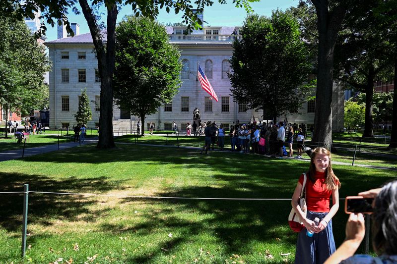 © Reuters. FILE PHOTO: A passerby poses for a photo with a Harvard tour group and the statue of John Harvard in the background on Harvard Yard, on the first day of the fall semester at Harvard University in Cambridge, Massachusetts, U.S., September 3, 2024.  REUTERS/Nicholas Pfosi/File Photo