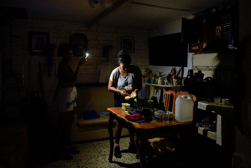 © Reuters. A woman prepares food with the aid of a cell phone light as Cuba is hit by an island-wide blackout, in Havana, Cuba, October 18, 2024. REUTERS/Norlys Perez