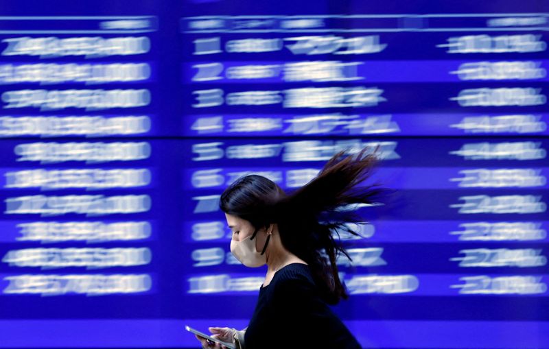 © Reuters. A passerby walks past an electric monitor displaying recent movements of various stock prices outside a bank in Tokyo, Japan, March 22, 2023. REUTERS/Issei Kato/File Photo